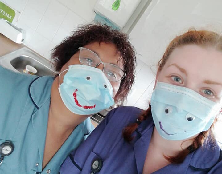 Two carers pose with smiley faces drawn on their face masks