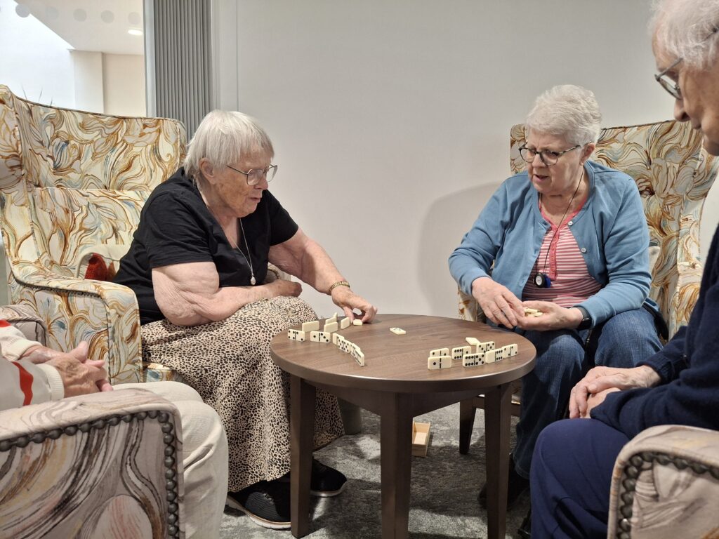 Group of people playing a tile game together in a communal lounge at a care home or supported living service.